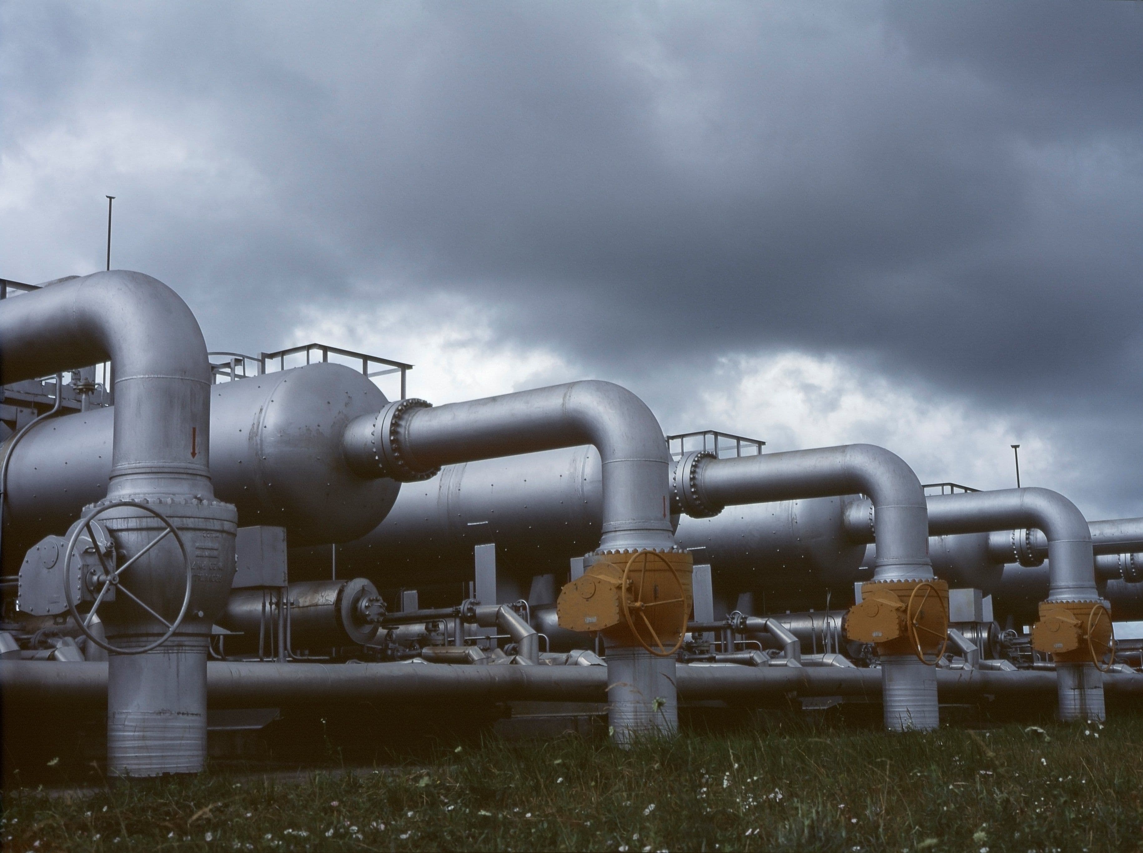 Insulated steel pipework and valves at a processing plant under a cloudy sky